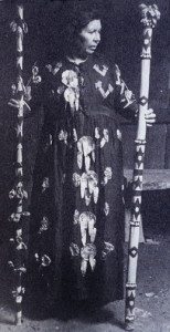 Essie Parrish holding sacred staffs with pendants.. She was the Yomta ("Song," a medicine woman's title) of the Kashaya Pomo. Her ceremonial dress is adorned with abalone pendants.